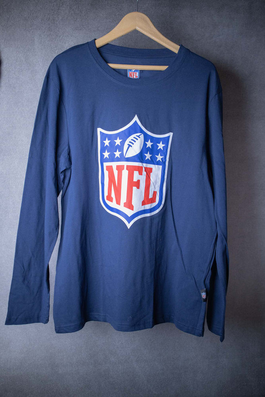 تیشرت آستین بلند مردانه سرمهای برند NFL با چاپ بزرگ لوگوی شیلد در نمای فلت لی (Flat Lay)